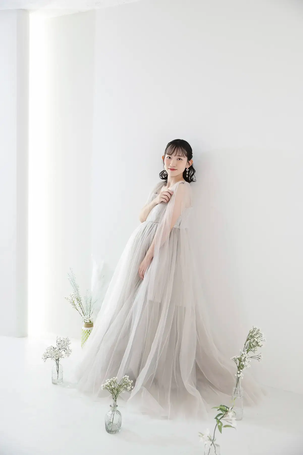 淡いグレーの衣装を着て花を持ったマタニティの女性