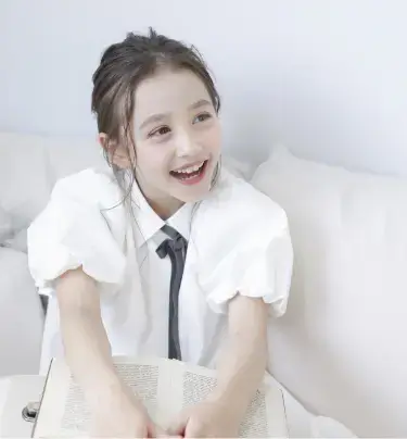 白いシャツ姿で本を手に微笑む小学生の女の子