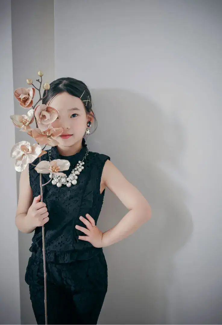 大ぶりのアクセサリーをつけた女の子が花を持って立つシックな雰囲気のポートレート