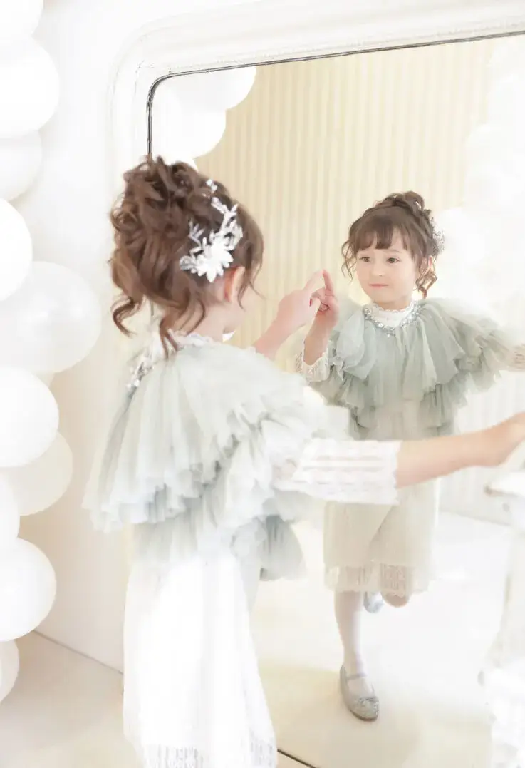 大きな鏡を見つめるおしゃれなドレス姿の女の子の記念写真