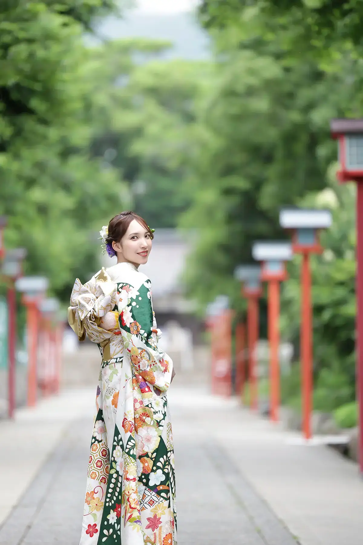 緑に囲まれた参道で振袖姿の女性がほほえむ成人式撮影