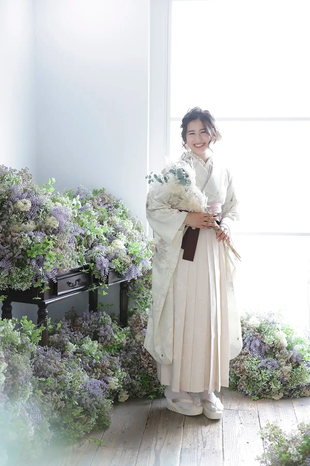 窓辺で白い袴姿の女性が花束を持ち笑顔を見せる卒業袴の記念撮影