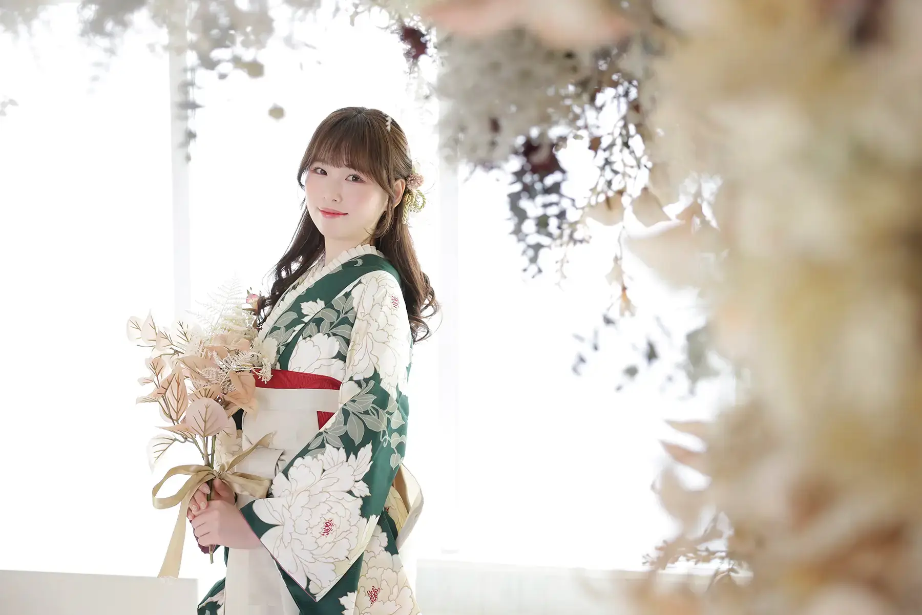 緑の着物にアイボリーの袴姿で花束を持つ女性の明るく上品な卒業袴写真
