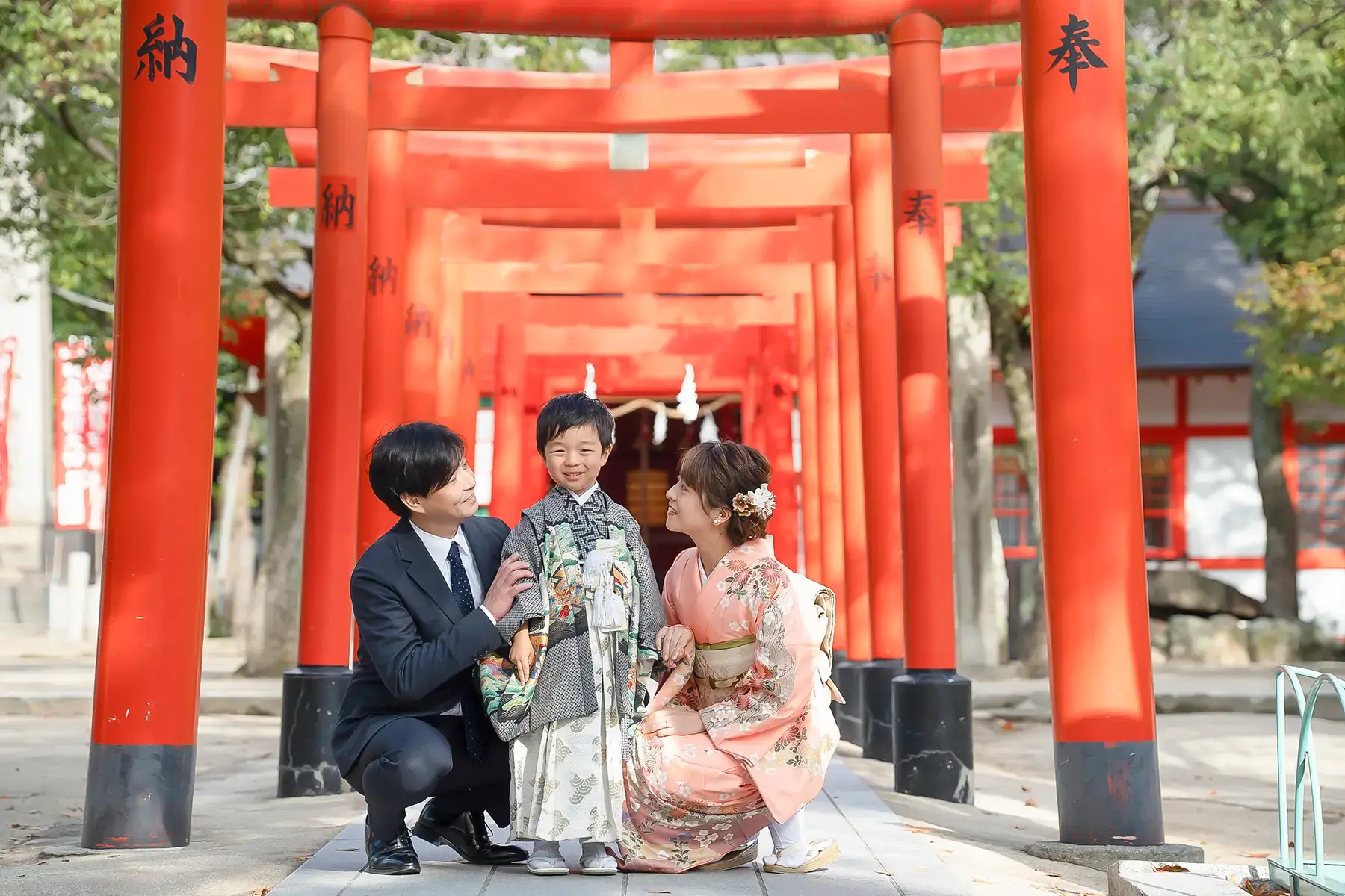 赤い鳥居の前で記念撮影をする着物姿の家族と笑顔の男の子|お宮参り写真」