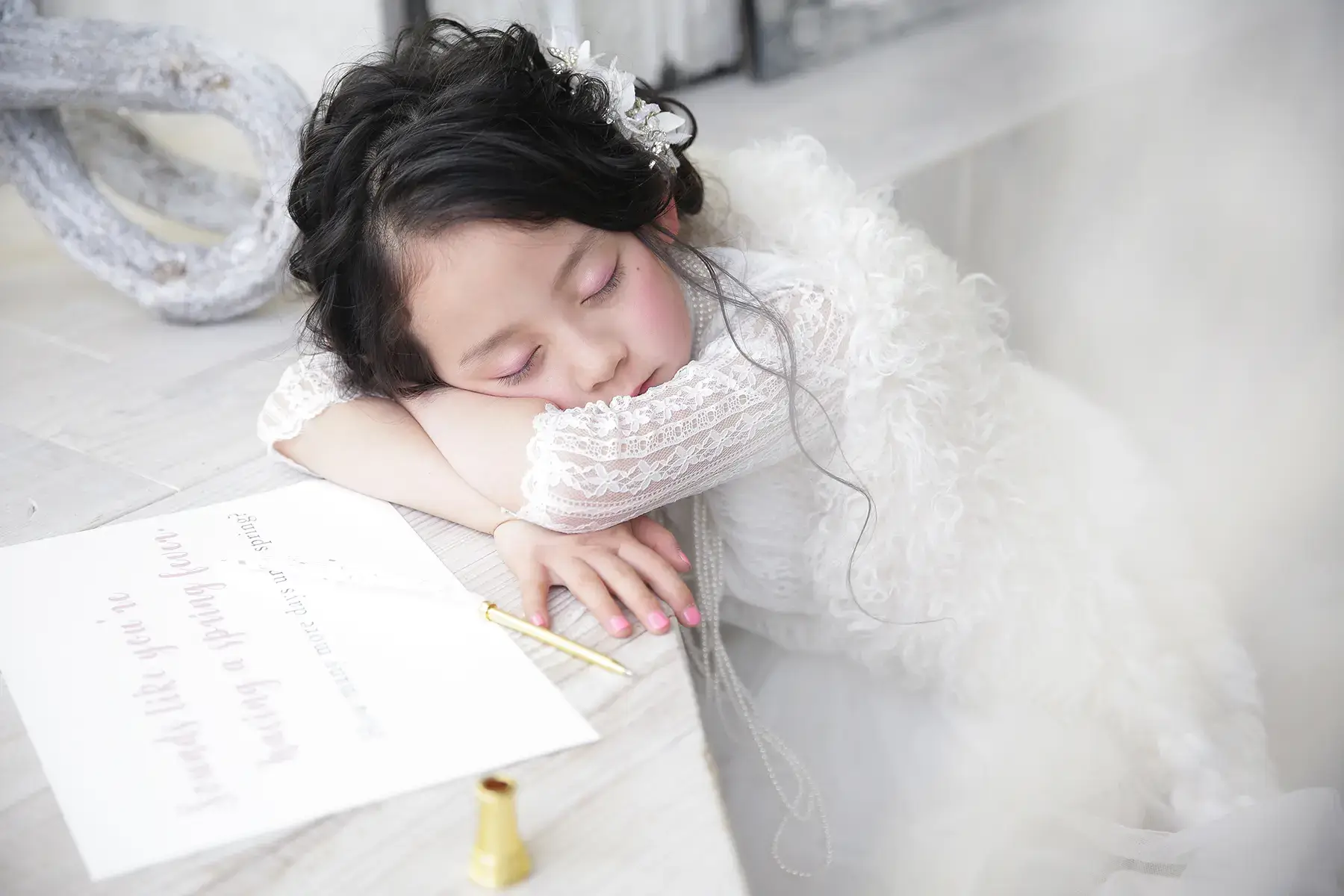 神戸で入学記念撮影をした女の子がレースのドレス姿で机に寄りかかって眠っている姿