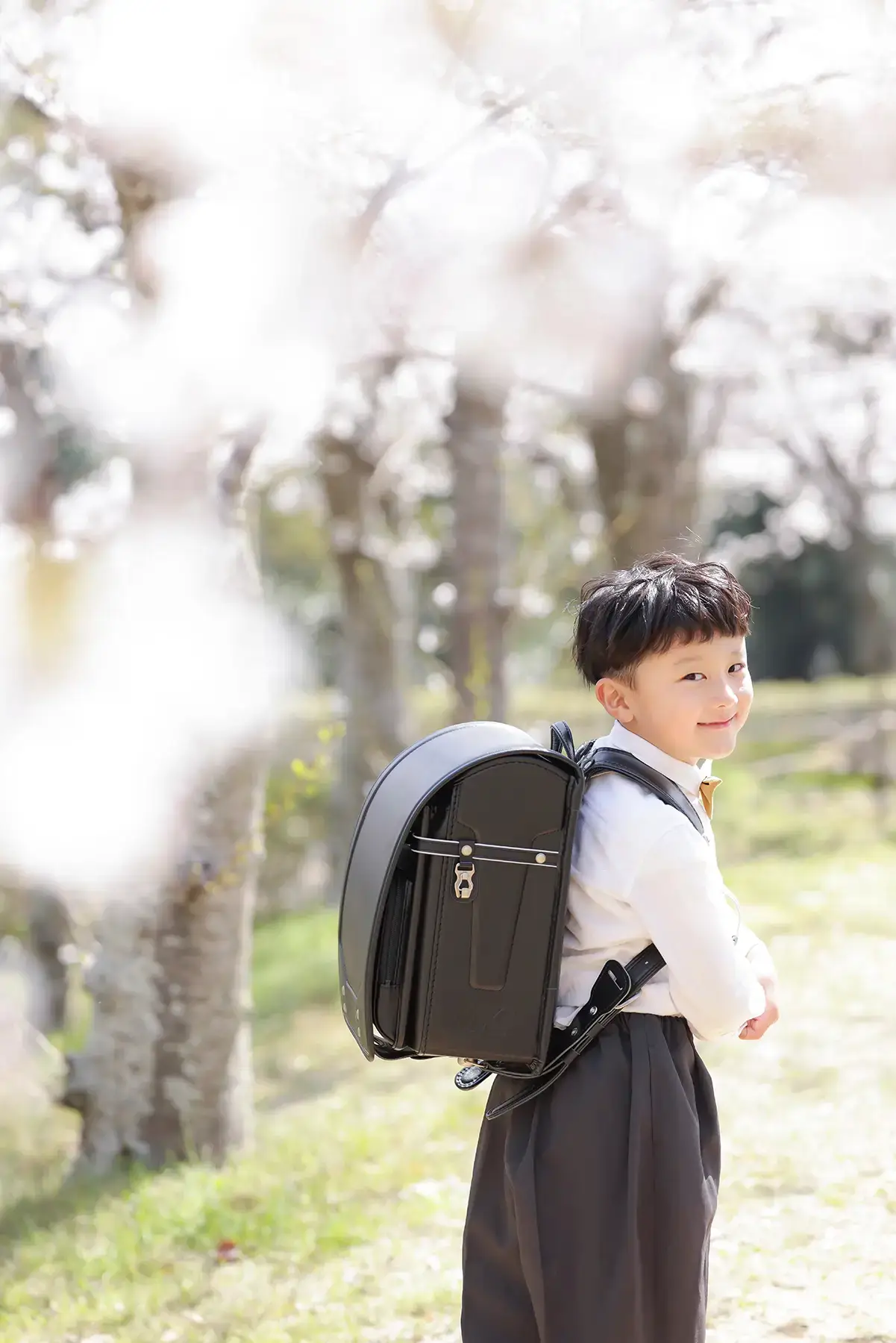 桜の木の前でランドセルを背負って微笑む男の子