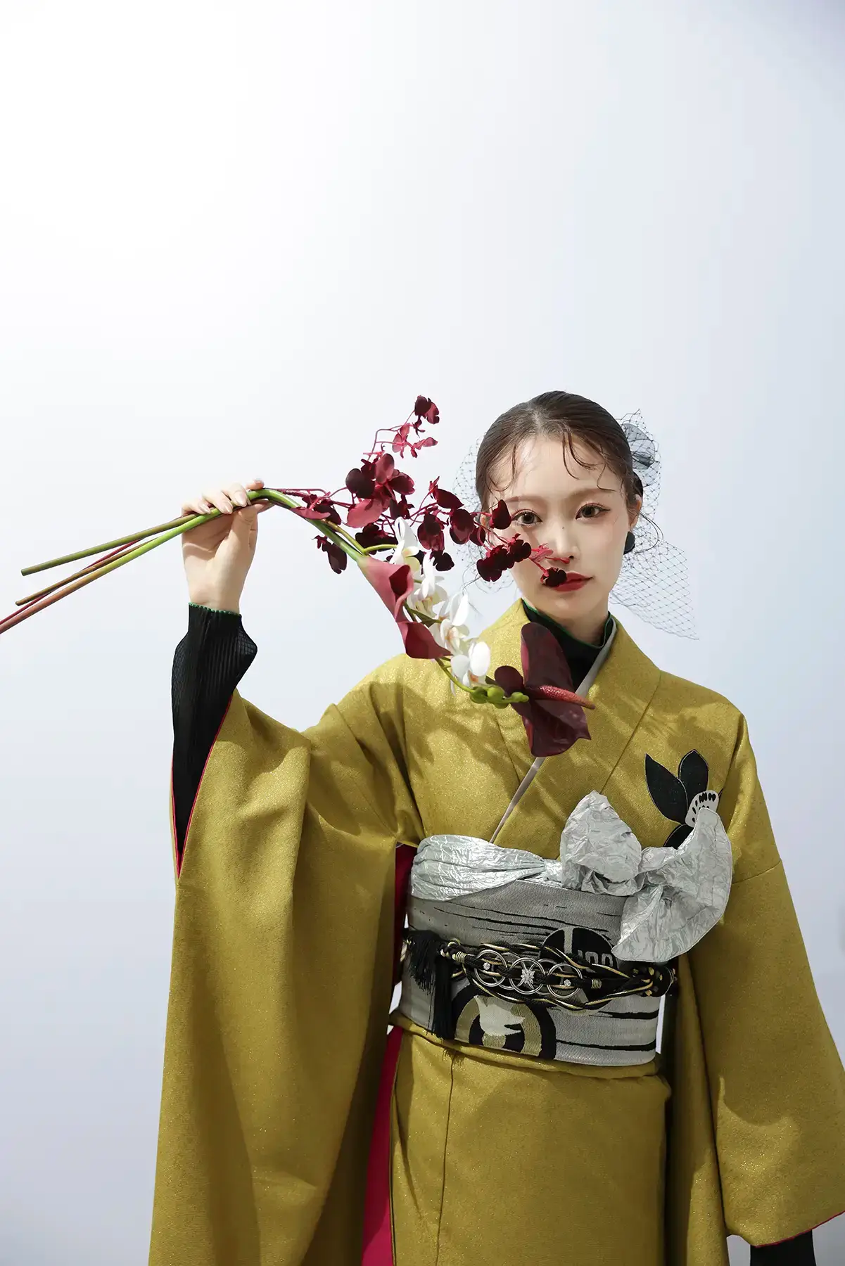 ゴールドの振袖を着た女性が赤い花を顔の前にかざす印象的な成人式記念写真
