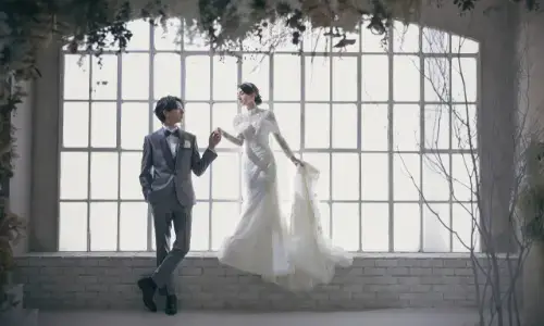 大きな窓の前でポーズをとるウェディングフォトの新郎新婦