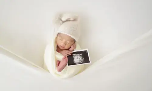 エコー写真を持って眠る帽子姿の新生児の記念フォト