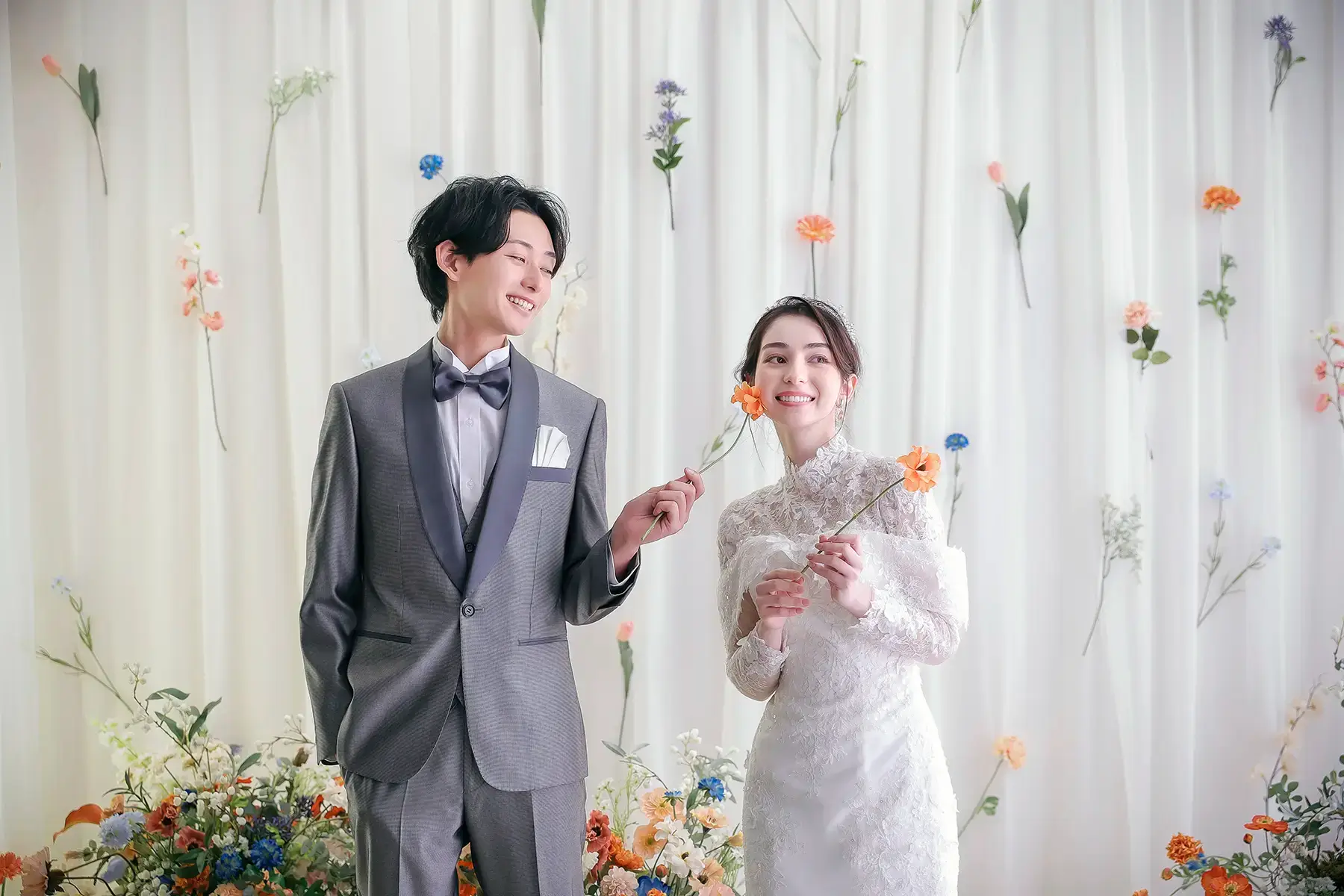 色とりどりの花を手に微笑む洋装カップルの明るいショット