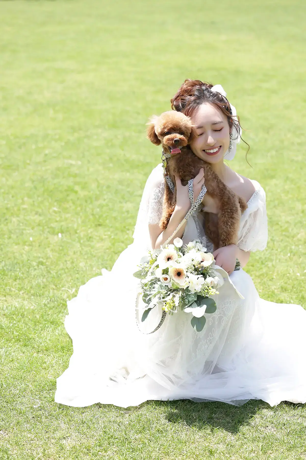 芝生の上で愛犬を抱く花嫁の笑顔が印象的なウェディングロケーションショット